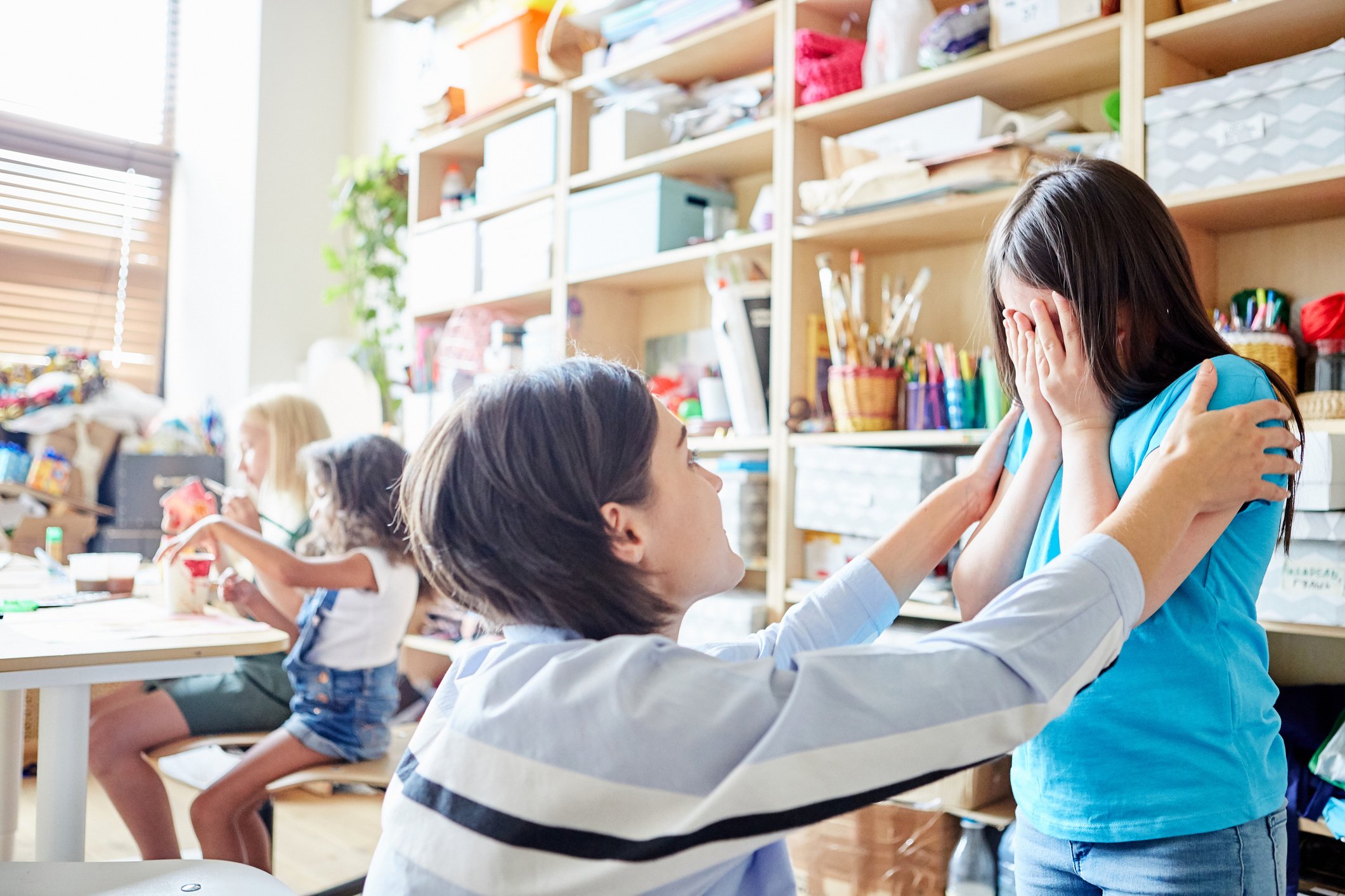 Educator comforting a child in a classroom setting, highlighting empathy and care.