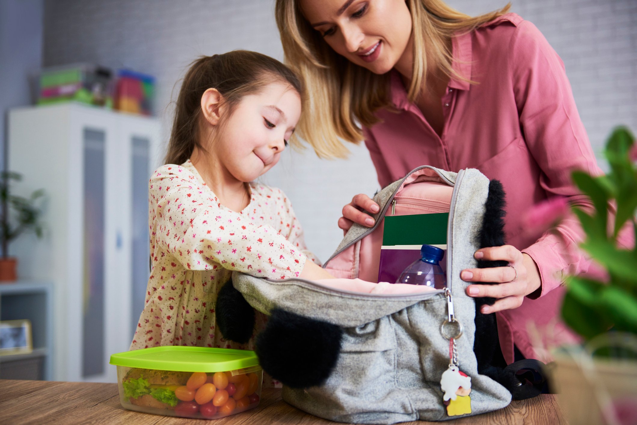 Parent helping young child pack a school backpack and lunch at home before school childcare.